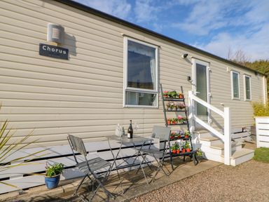 A small outdoor seating area with a metal table and chairs and a plant stand with flowers beside a beige mobile home at 46 Willowburn in Felton