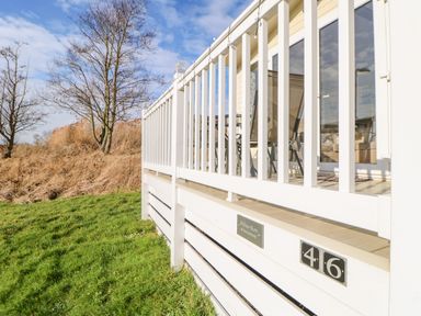 A patio with white railing chairs and a glass door overlooking grass and trees at 46 Willowburn Felton
