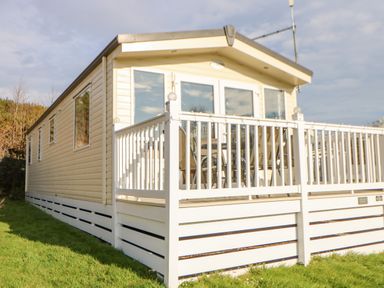 A beige mobile home with white railing and outdoor chairs on a deck at 46 Willowburn in Felton