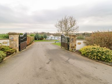 A driveway with open black iron gates between stone pillars leading to a road with a trailer and trees at 46 Willowburn in Felton