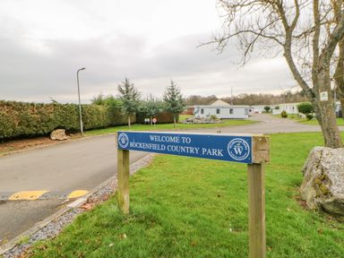 A blue sign with welcome to bockenfield country park near a road with speed bumps and trees