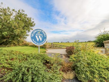 Outdoor view of a Wyldecrest Parks Holiday sign surrounded by bushes and trees at 46 Willowburn in Felton