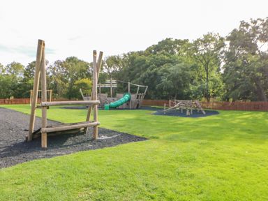 An outdoor playground with wooden climbing structures and a green slide on grass at 46 Willowburn in Felton