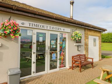 The entrance of Timeout Tavern with glass doors a wooden bench two hanging flower baskets and outdoor picnic tables at 46 Willowburn Felton
