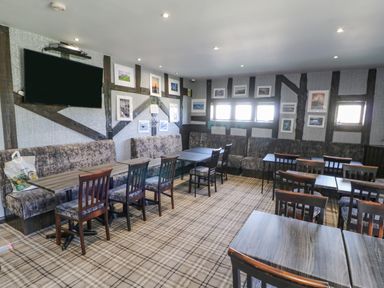 A dining area with tables and chairs along a wall with framed pictures and a mounted television at 46 Willowburn in Felton