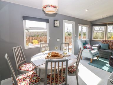 A dining area with a round table set with glasses and bread and chairs with patterned cushions next to a living room with armchairs and a sofa at Cwrt y Ceffyl in Boduan near Morfa Nefyn