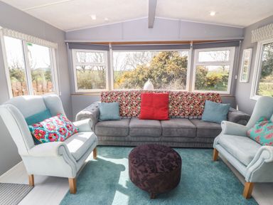 A living room with a gray sofa and two light blue armchairs with colorful pillows and a round dark ottoman on a light blue carpet at Cwrt y Ceffyl in Boduan near Morfa Nefyn