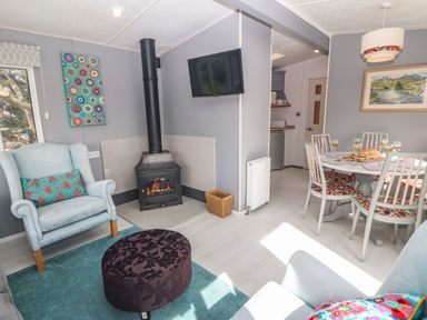 A living room with armchairs a fireplace a wall-mounted television and a dining area with a table and chairs at Cwrt y Ceffyl in Boduan near Morfa Nefyn