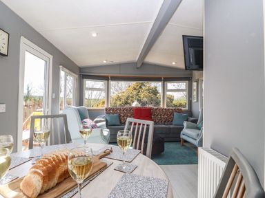 A dining table with glasses of white wine and sliced bread near a seating area with armchairs and a sofa at Cwrt y Ceffyl in Boduan near Morfa Nefyn