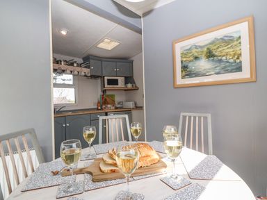 A dining table set with six glasses of white wine and sliced bread on a wooden board in a room with grey walls and kitchen cabinets at Cwrt y Ceffyl in Boduan near Morfa Nefyn