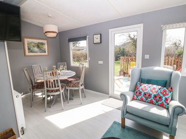 A dining area with six chairs around a round table and an armchair near a glass door at Cwrt y Ceffyl in Boduan near Morfa Nefyn