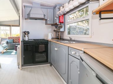 A kitchen with a black stove gray cabinets a sink and a window showing a stone wall outside at Cwrt y Ceffyl in Boduan near Morfa Nefyn