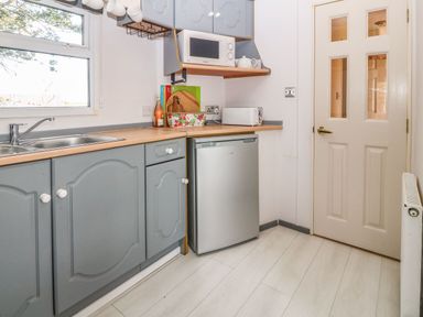 A kitchen with blue cabinets a microwave toaster mini fridge and a sink next to a window at Cwrt y Ceffyl Boduan near Morfa Nefyn