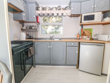 A kitchen with grey cabinets a stove a sink a refrigerator a microwave and pots above the sink at Cwrt y Ceffyl in Boduan near Morfa Nefyn