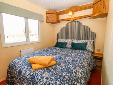 A bedroom with a bed with floral bedding and green pillows under wooden cabinets with a window on the side at Cwrt y Ceffyl in Boduan near Morfa Nefyn