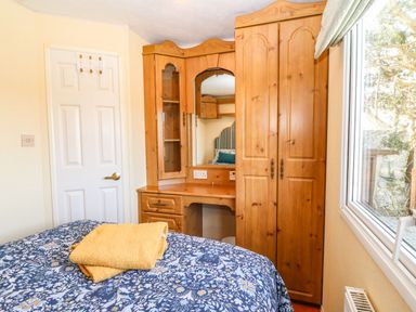 A bedroom with a wooden wardrobe and dressing table beside a window with yellow towels on a blue patterned bedspread at Cwrt y Ceffyl in Boduan near Morfa Nefyn