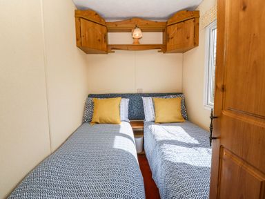 A small bedroom with two single beds with patterned bedspreads and yellow pillows under wooden cupboards at Cwrt y Ceffyl in Boduan near Morfa Nefyn
