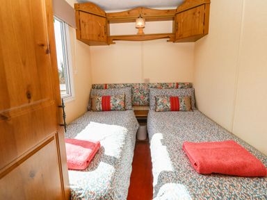 A small bedroom with two single beds with patterned bedding and red towels a wooden cabinet and a window at Cwrt y Ceffyl Boduan near Morfa Nefyn