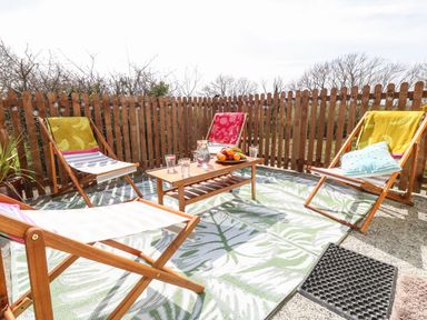 An outdoor patio with four wooden deck chairs around a wooden coffee table with a fruit plate and glasses near a wooden fence at Cwrt y Ceffyl in Boduan near Morfa Nefyn