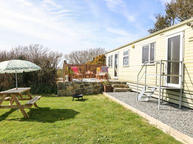 A garden area with a wooden picnic table and umbrella a small patio with chairs and a table next to a mobile home at Cwrt y Ceffyl in Boduan near Morfa Nefyn