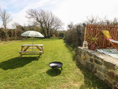 A garden with picnic table and umbrella a fire pit and a deck chair at Cwrt y Ceffyl in Boduan near Morfa Nefyn