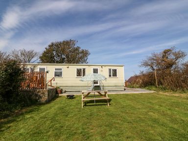 A mobile home with three windows in a grassy yard with a picnic table and umbrella at Cwrt y Ceffyl in Boduan near Morfa Nefyn