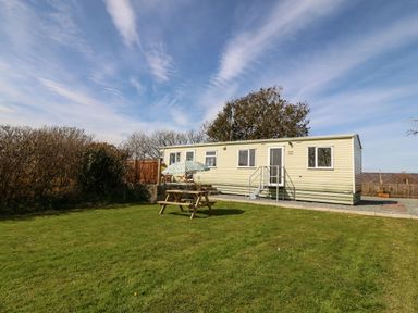 A mobile home with a picnic table and umbrella on a grassy lawn at Cwrt y Ceffyl in Boduan near Morfa Nefyn