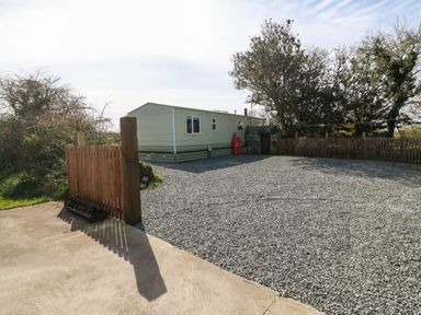 A gravel driveway with a small mobile home and wooden fences surrounded by trees at Cwrt y Ceffyl in Boduan near Morfa Nefyn