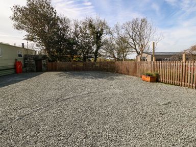 An outdoor area covered with gravel surrounded by a wooden fence and trees at Cwrt y Ceffyl in Boduan near Morfa Nefyn