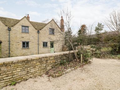 An exterior view of a stone house with a gravel driveway and a low stone wall at High Cogges Farm Holiday Cottages Witney
