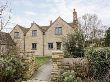 Stone cottage with multiple windows and a green door behind a stone wall garden at High Cogges Farm Holiday Cottages in Witney