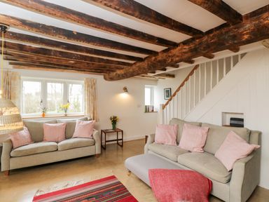 A living room with two sofas with pink cushions a staircase and wooden ceiling beams at High Cogges Farm Holiday Cottages in Witney