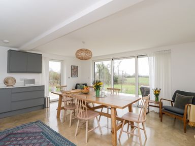 A dining area with a wooden table and chairs next to large windows overlooking a field at High Cogges Farm Holiday Cottages in Witney