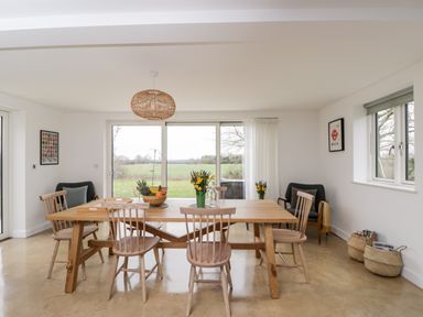 A dining room with a wooden table and chairs next to large windows showing a field at High Cogges Farm Holiday Cottages Witney