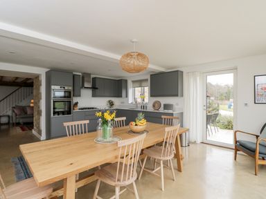 A kitchen and dining area with a wooden table and chairs gray cabinets and a glass door at High Cogges Farm Holiday Cottages Witney