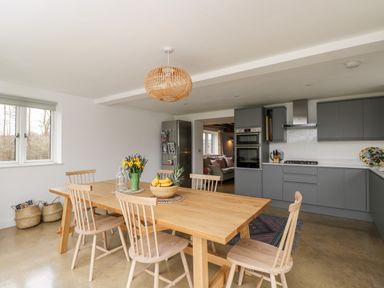 A kitchen with gray cabinets a wooden dining table with chairs and a fruit bowl at High Cogges Farm Holiday Cottages Witney