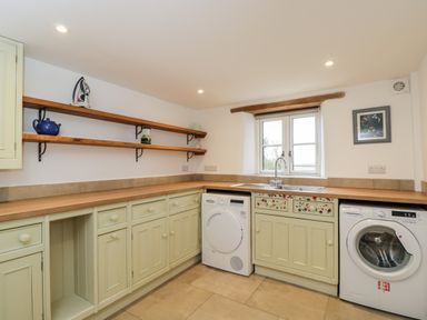 A utility room with a washing machine dryer sink wooden shelves and cabinets at High Cogges Farm Holiday Cottages in Witney