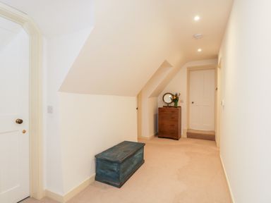 A hallway with beige carpet a wooden chest and a chest of drawers with a mirror and flowers at High Cogges Farm Holiday Cottages in Witney