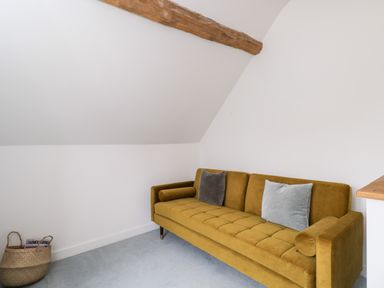 A room with a mustard yellow sofa with two cushions and a basket with magazines on the floor at High Cogges Farm Holiday Cottages Witney