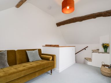 A room with a mustard-colored sofa cushions wooden ceiling beams stairs with stone steps and a basket at High Cogges Farm Holiday Cottages Witney