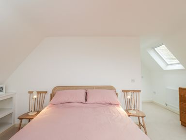 A bedroom with a bed with pink bedding and wooden chairs as bedside tables with lamps at High Cogges Farm Holiday Cottages in Witney