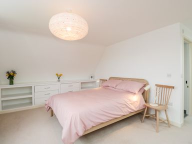 A bedroom with a bed with pink bedding a wooden chair with a lamp on it and built in white shelves at High Cogges Farm Holiday Cottages Witney