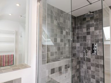 A bathroom shower area with gray tiled walls and a glass partition at High Cogges Farm Holiday Cottages Witney