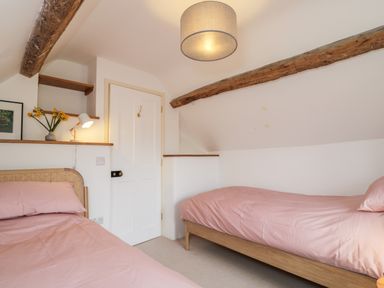 A bedroom with two single beds with pink bed linens wooden beams and a white door at High Cogges Farm Holiday Cottages Witney