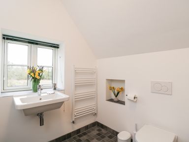 A bathroom with a sink under a window and flowers on the windowsill at High Cogges Farm Holiday Cottages in Witney