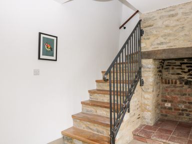A staircase with wooden steps and black metal railing next to a brick fireplace with a stone wall at High Cogges Farm Holiday Cottages Witney