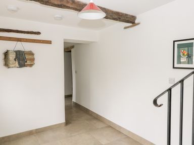 A hallway with beige tiled floor a wooden beam on the ceiling a metal handrail and framed bird picture on the wall at High Cogges Farm Holiday Cottages Witney