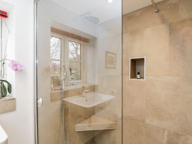 A shower area with beige tiles including a built-in shelf and a corner seat at High Cogges Farm Holiday Cottages Witney