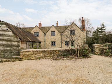 An exterior view of a stone cottage with chimneys a gravel driveway wooden shed and stone wall at High Cogges Farm Holiday Cottages Witney