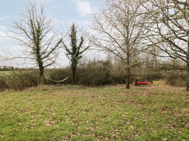 A grassy yard with trees a hammock and a red swing at High Cogges Farm Holiday Cottages in Witney
